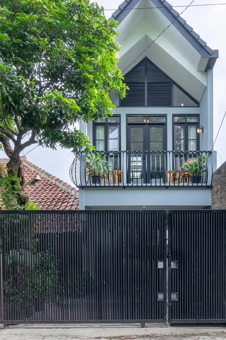 Villa exterior with pitched roof, balcony and private gated entrance framed by a mature mango tree