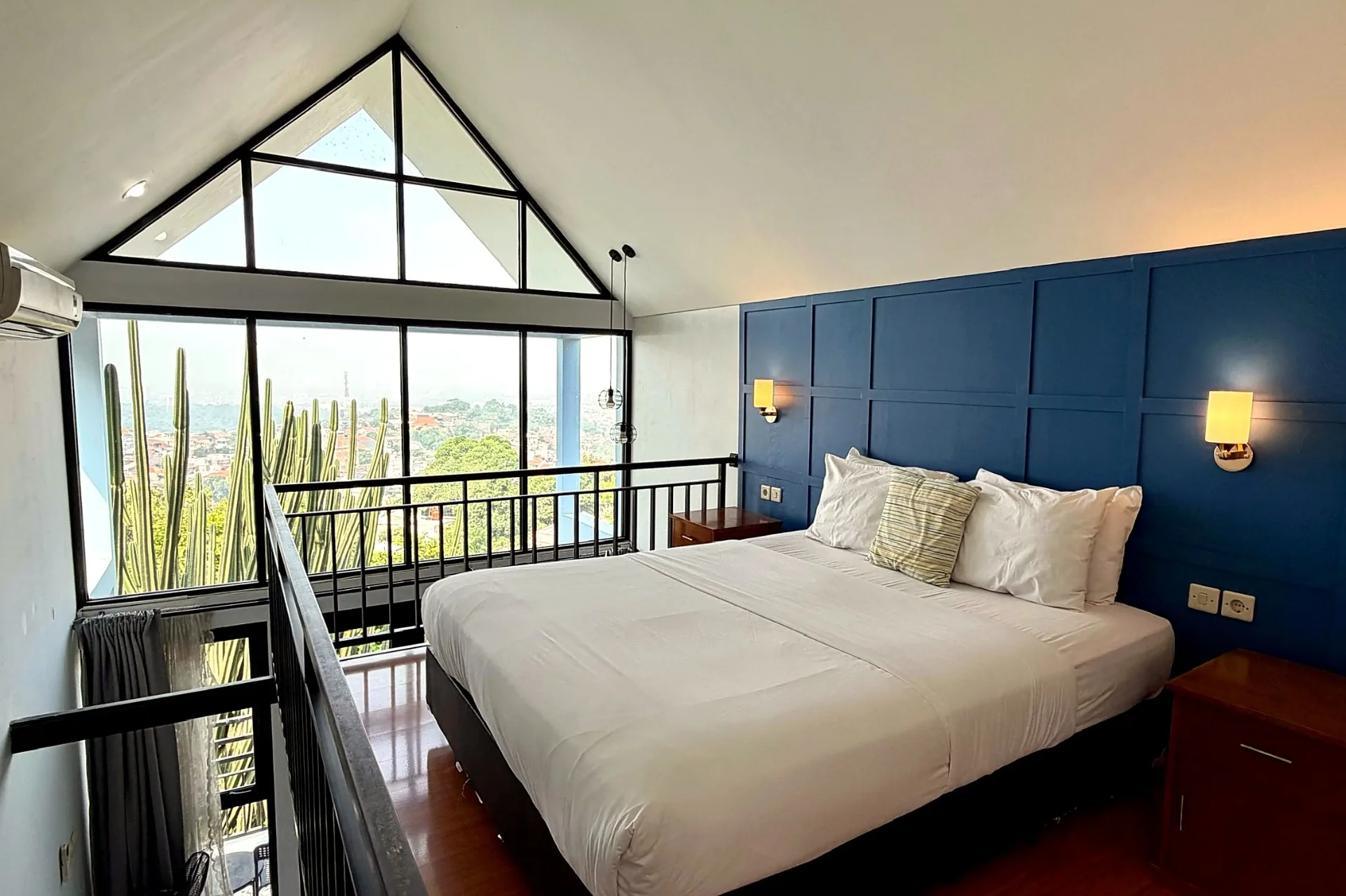 Mezzanine bedroom with blue feature wall, queen bed and pitched picture windows overlooking Bandung
